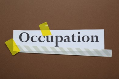 Photo of Word Occupation attached with yellow adhesive tape on brown background