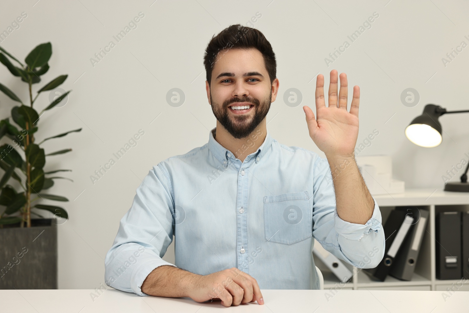 Photo of Happy young man waving hello during video chat indoors, view from web camera