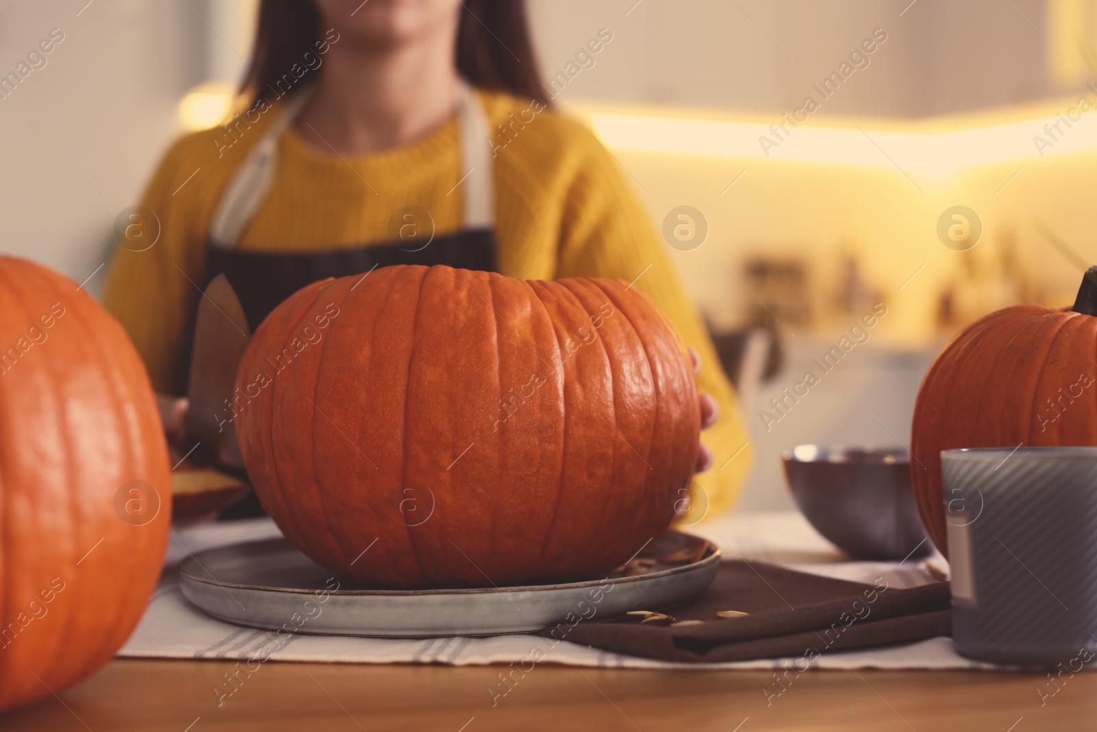 Photo of Woman carving pumpkin at table in kitchen. Halloween celebration