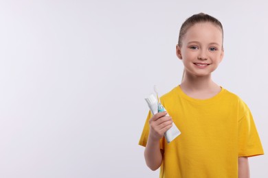 Photo of Happy girl holding electric toothbrush and tube of toothpaste on white background. Space for text