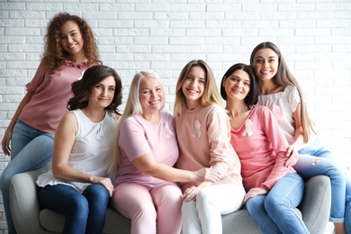 Group of women with silk ribbons sitting on sofa against brick wall. Breast cancer awareness concept