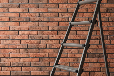 Photo of Metal step ladder near brick wall, closeup. Space for text