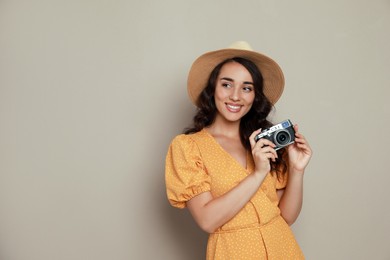 Beautiful young woman with straw hat and camera on beige background. Space for text
