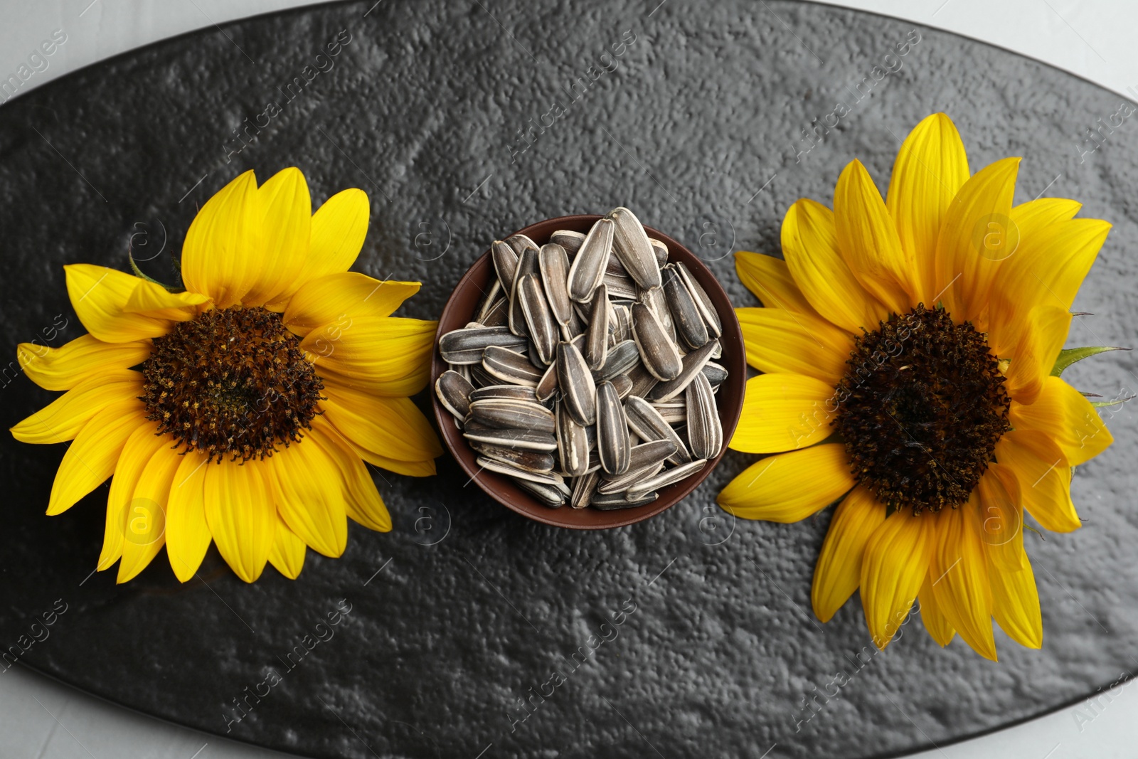 Photo of Raw sunflower seeds and flowers on slate board, flat lay