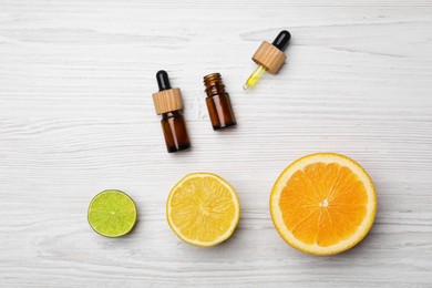 Photo of Bottles of citrus essential oils and fresh fruits on white wooden table, flat lay