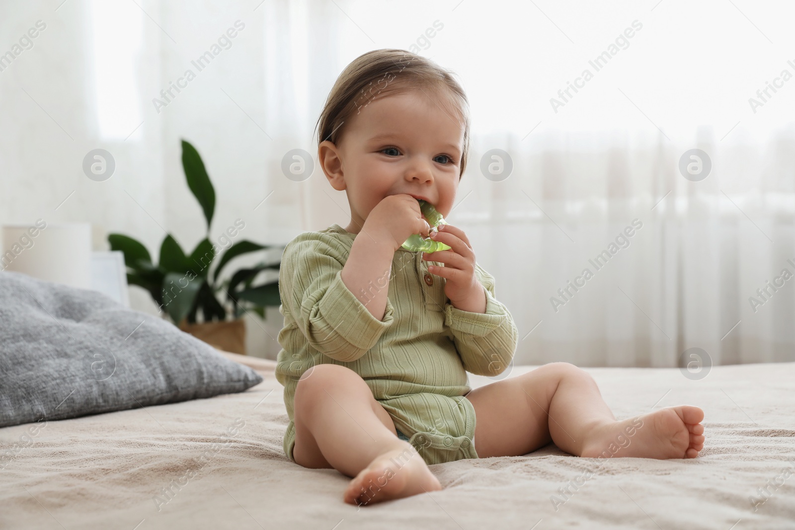 Photo of Cute baby girl with teething toy on bed at home