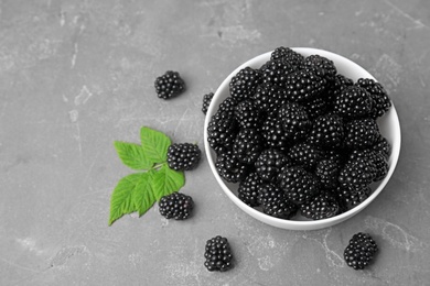 Bowl with ripe blackberries and leaves on grey table
