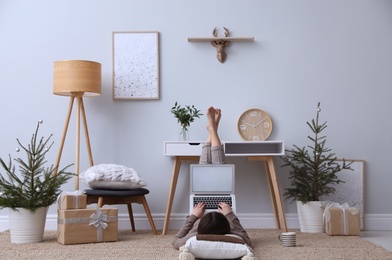 Woman using laptop in room decorated with potted fir trees