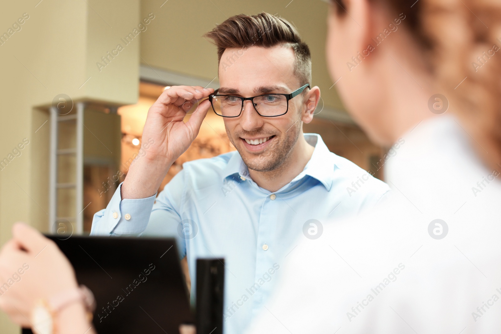 Photo of Female ophthalmologist helping man to choose glasses in optical store