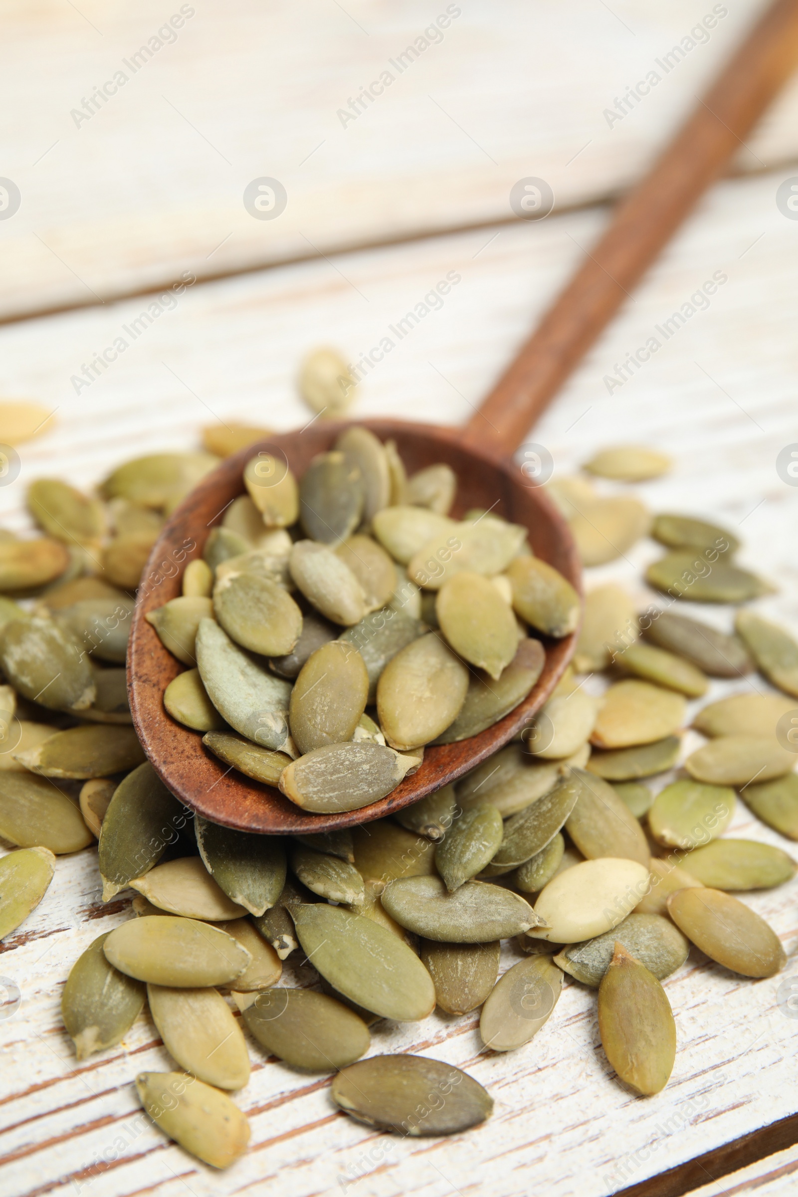 Photo of Spoon with pumpkin seeds on white wooden table, closeup