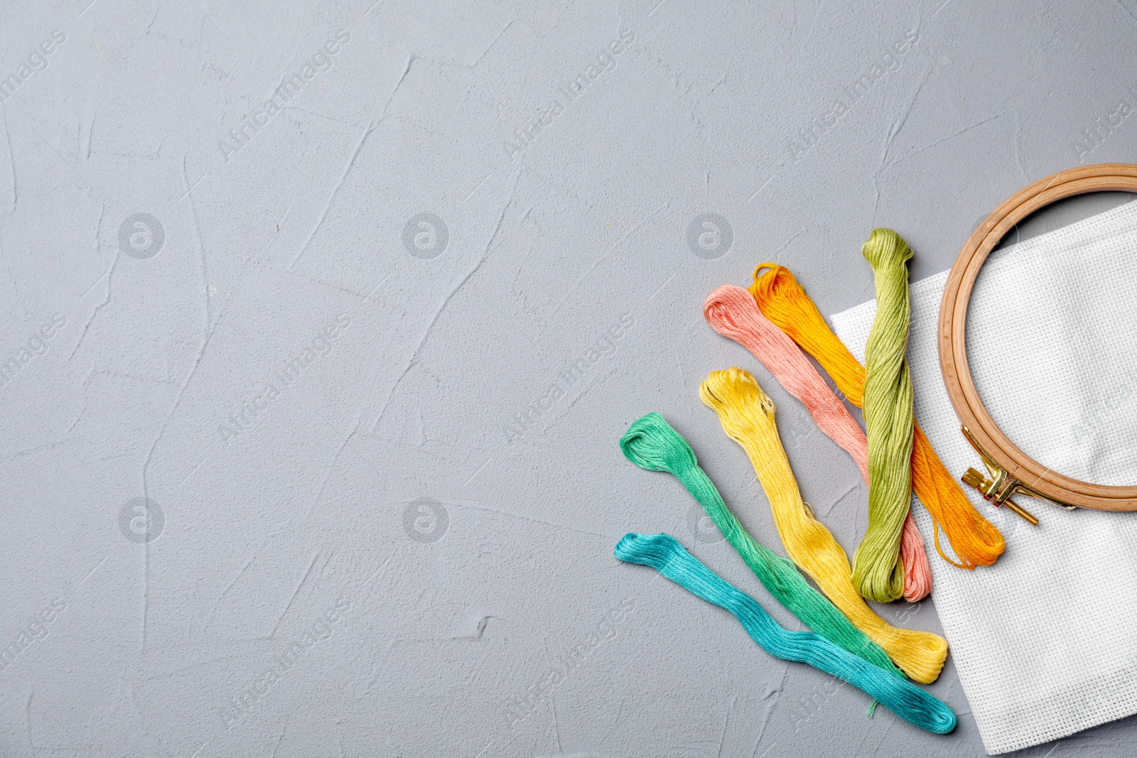 Photo of Color sewing threads, hoop and fabric on gray background, top view