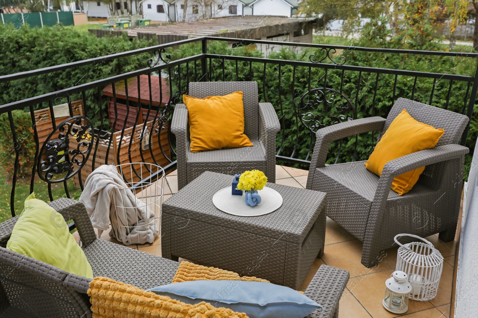 Photo of Colorful pillows, soft blanket and yellow chrysanthemum flowers on rattan garden furniture outdoors