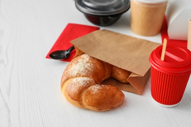 Paper bag with pastry and takeaway food on wooden table. Space for text