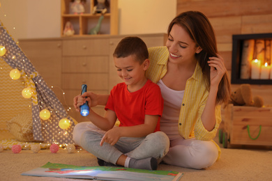Mother and son with flashlight reading book at home