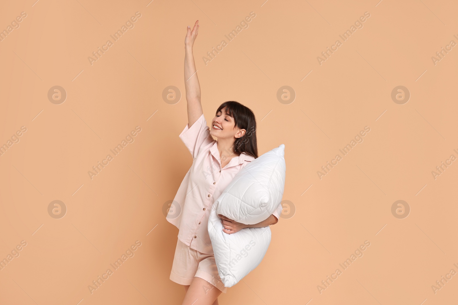 Photo of Happy woman wearing pyjama and holding pillow on beige background