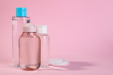Photo of Bottles of micellar water and cotton pads on pink background. Space for text