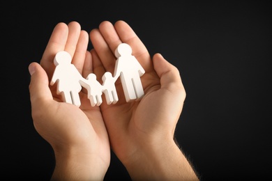 Photo of Man holding figure of family in hands on black background, closeup