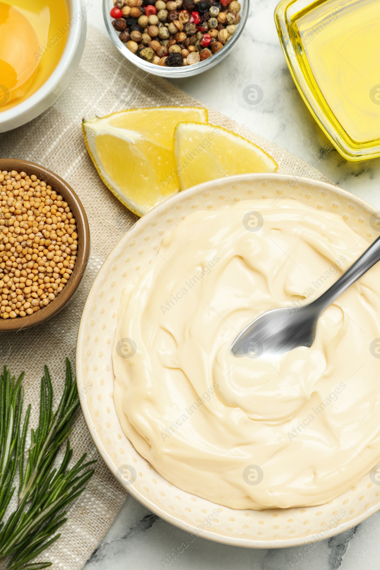 Photo of Bowl with fresh mayonnaise and ingredients on white marble table, flat lay