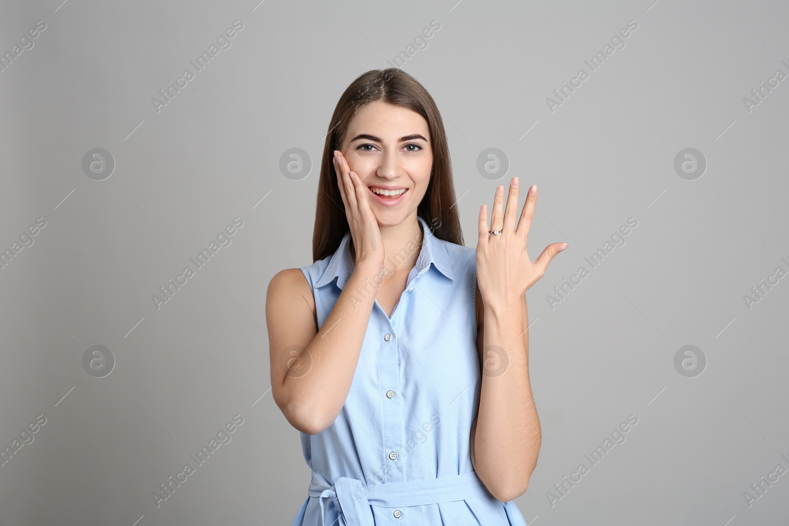 Photo of Happy young woman wearing beautiful engagement ring on grey background