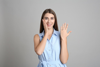 Happy young woman wearing beautiful engagement ring on grey background