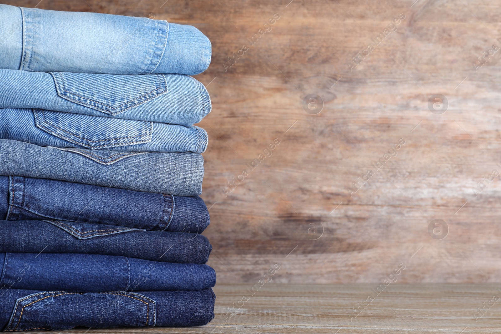 Photo of Stack of different jeans on wooden table. Space for text