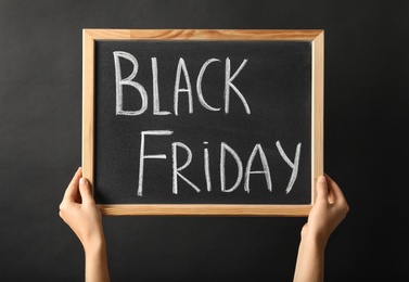 Photo of Woman holding chalkboard with words Black Friday against dark background, closeup