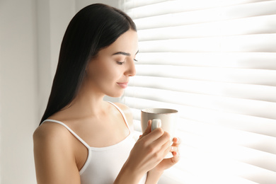 Photo of Young woman with cup of tea near window. Lazy morning