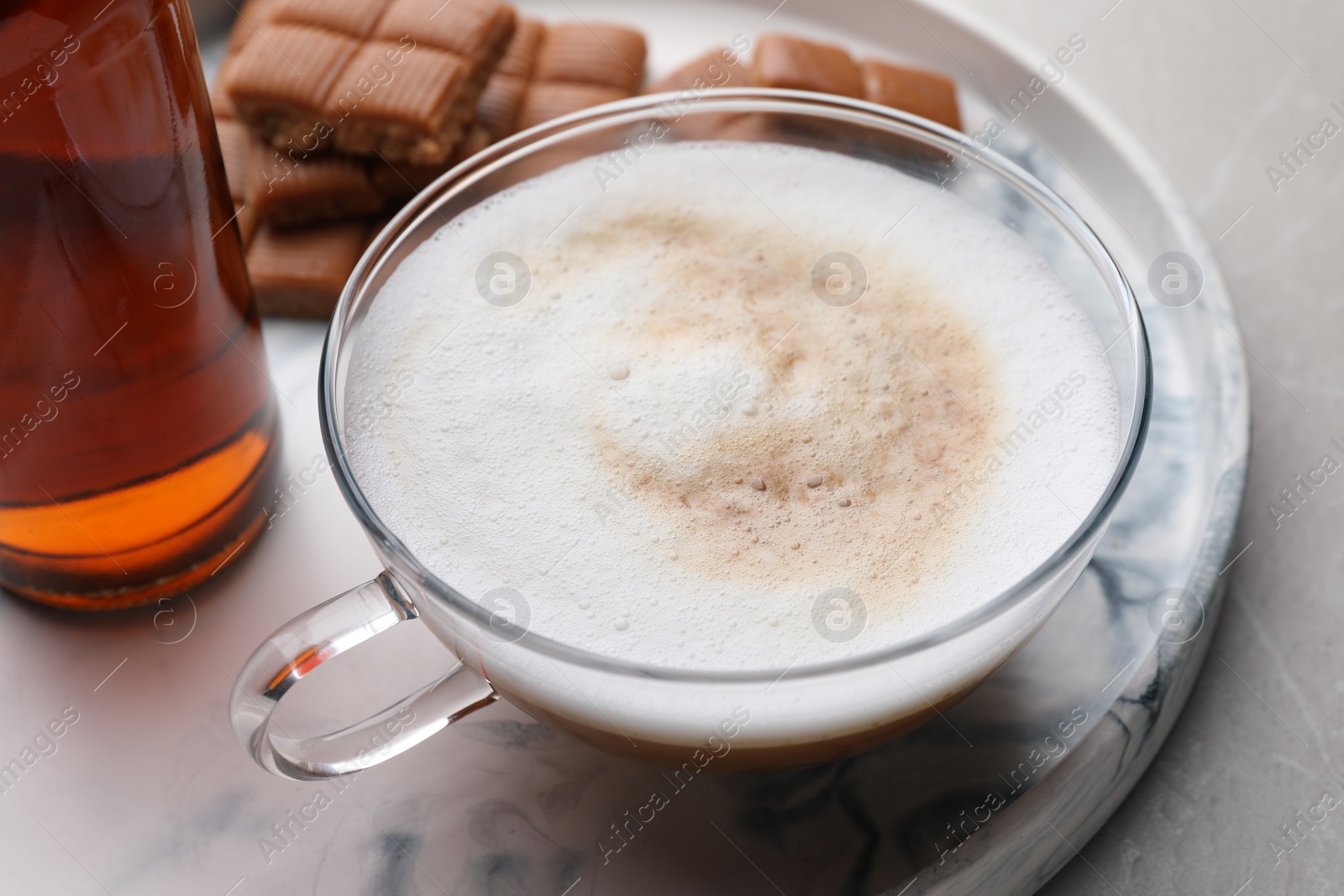 Photo of Bottle of delicious syrup, glass of coffee and caramel candies on grey table, closeup