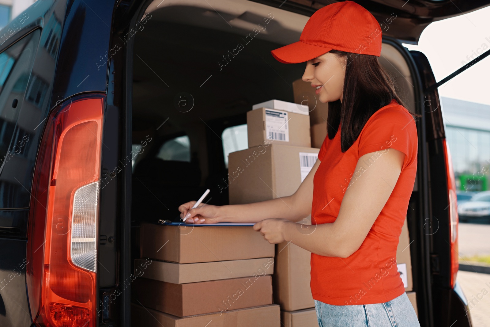 Photo of Courier with clipboard checking packages near delivery van outdoors