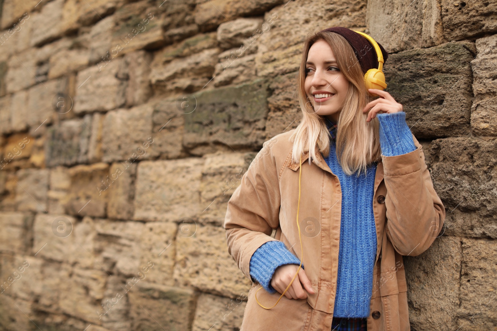 Photo of Young woman with headphones listening to music near stone wall. Space for text