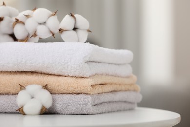 Photo of Terry towels and cotton branch with fluffy flowers on white table indoors, closeup. Space for text