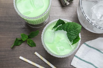 Photo of Delicious mint liqueur with green leaves and ice cubes on grey wooden table, flat lay