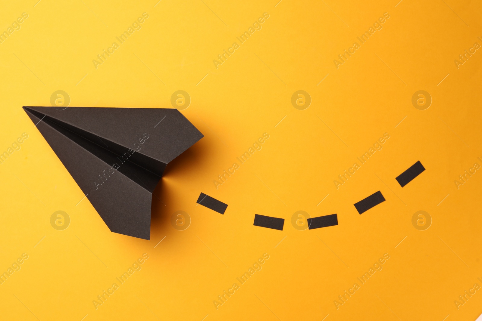 Photo of Handmade black paper plane with dotted lines on yellow background, top view