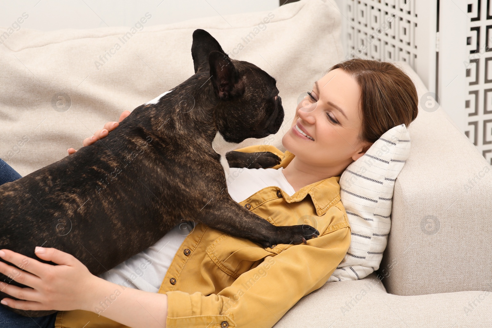 Photo of Happy woman with cute French Bulldog on soft sofa in room