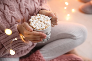 Photo of Woman holding cup of hot drink with marshmallows indoors, closeup. Magic Christmas atmosphere