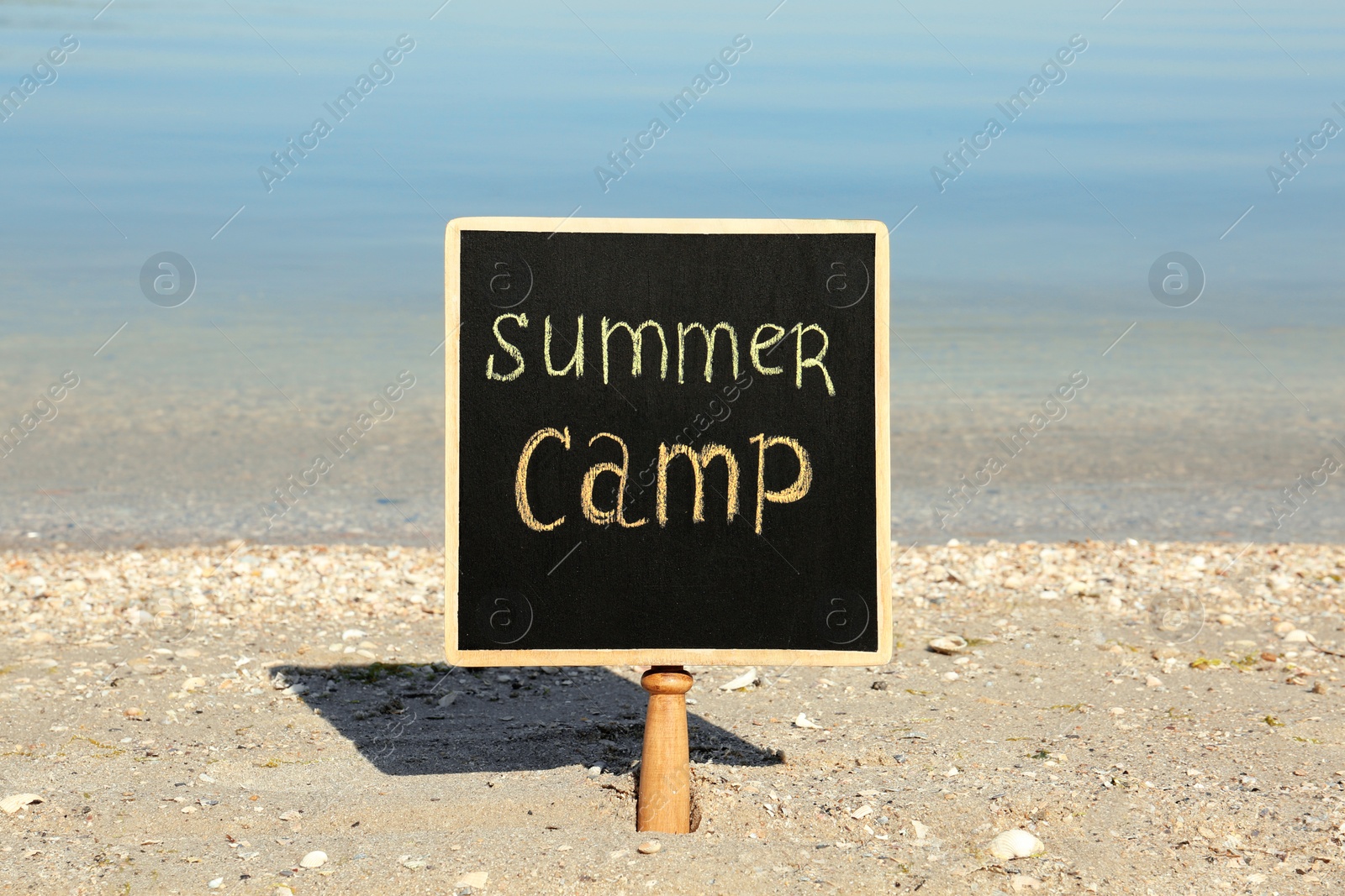 Photo of Small chalkboard with text SUMMER CAMP on beach near river