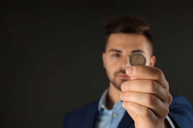 Photo of Young man holding coin against black background, focus on hand. Space for text