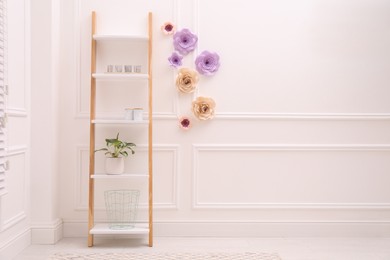 Shelving unit near wall with floral decor in room, space for text. Interior design