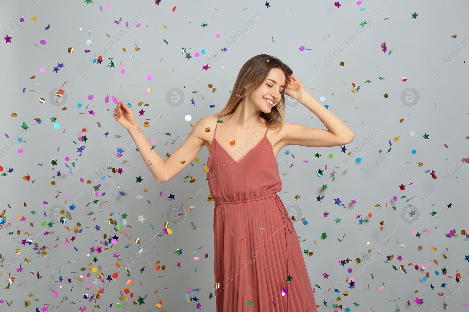 Photo of Happy woman and falling confetti on light grey background