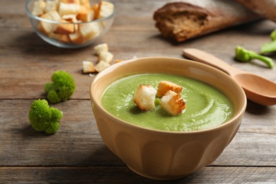 Photo of Bowl of broccoli cream soup with croutons served on wooden table