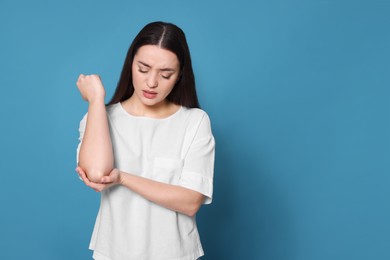 Photo of Young woman suffering from pain in elbow on light blue background. Arthritis symptoms