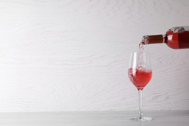 Pouring delicious rose wine into glass on table against white wooden background. Space for text