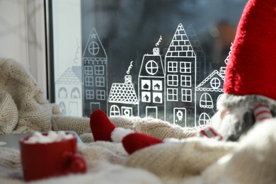 Photo of Gnome, laptop and hot drink on knitted plaid near window with beautiful drawing at home. Christmas decor
