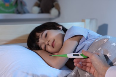 Photo of Doctor with thermometer near sick little boy in bed indoors