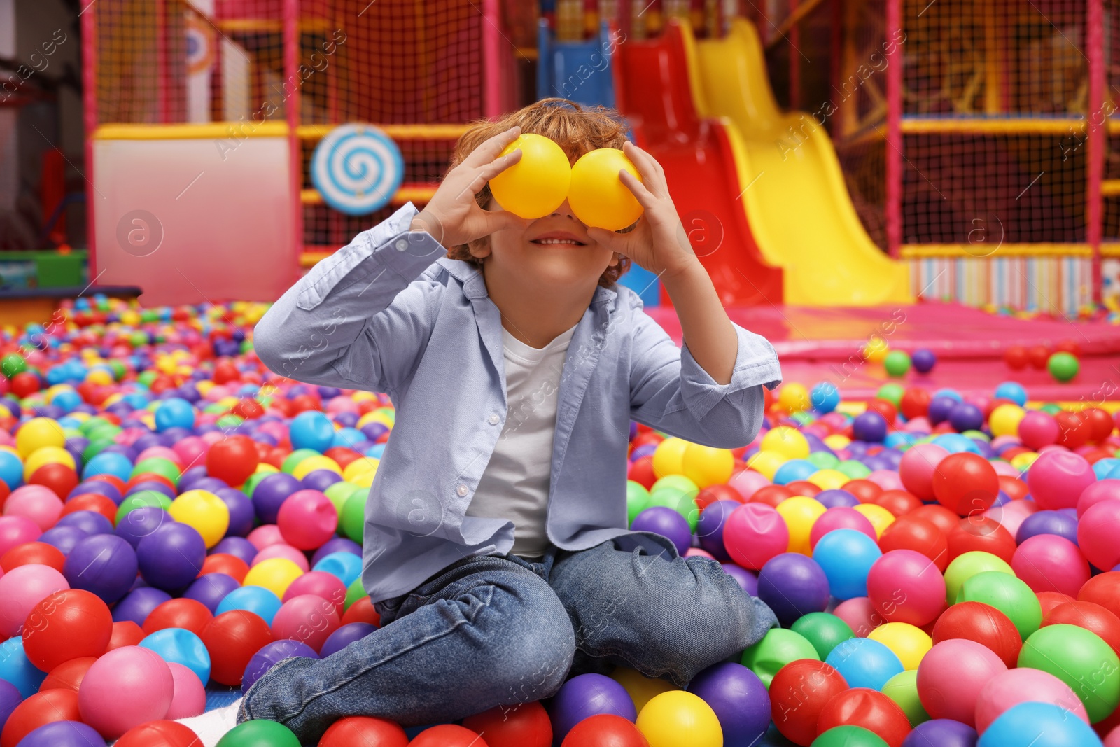 Photo of Happy little boy holding colorful balls in ball pit