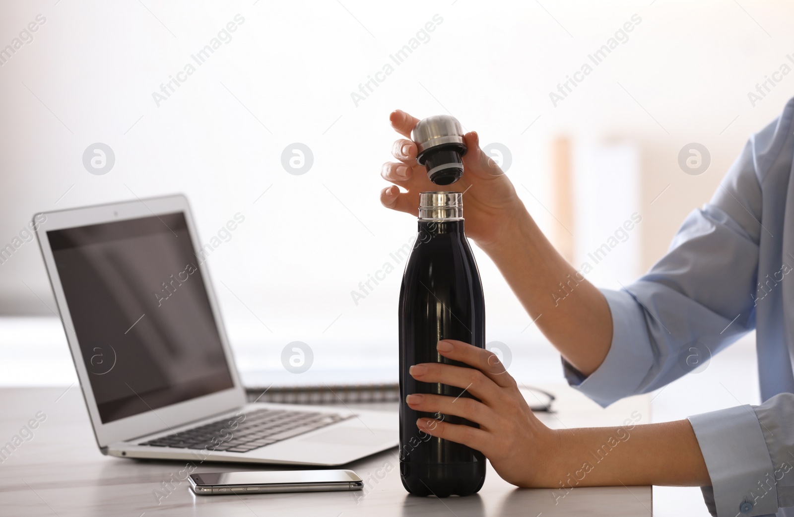 Photo of Woman with thermo bottle working at table in modern office, closeup