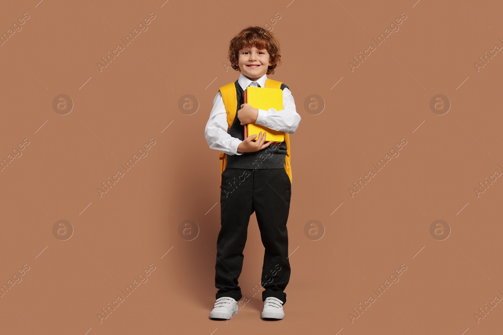 Photo of Happy schoolboy with backpack and books on brown background