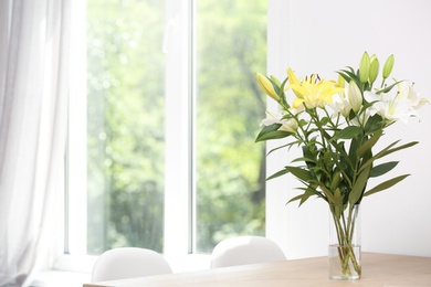 Vase with bouquet of beautiful lilies on wooden table indoors. Space for text