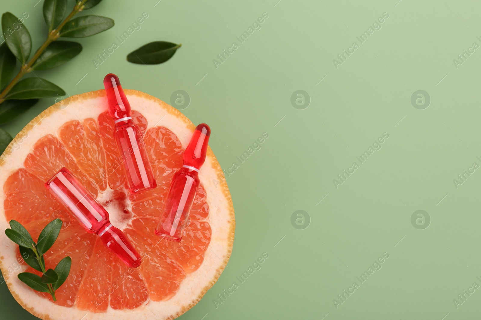 Photo of Skincare ampoules with vitamin C, half of grapefruit and leaves on light green background, flat lay. Space for text