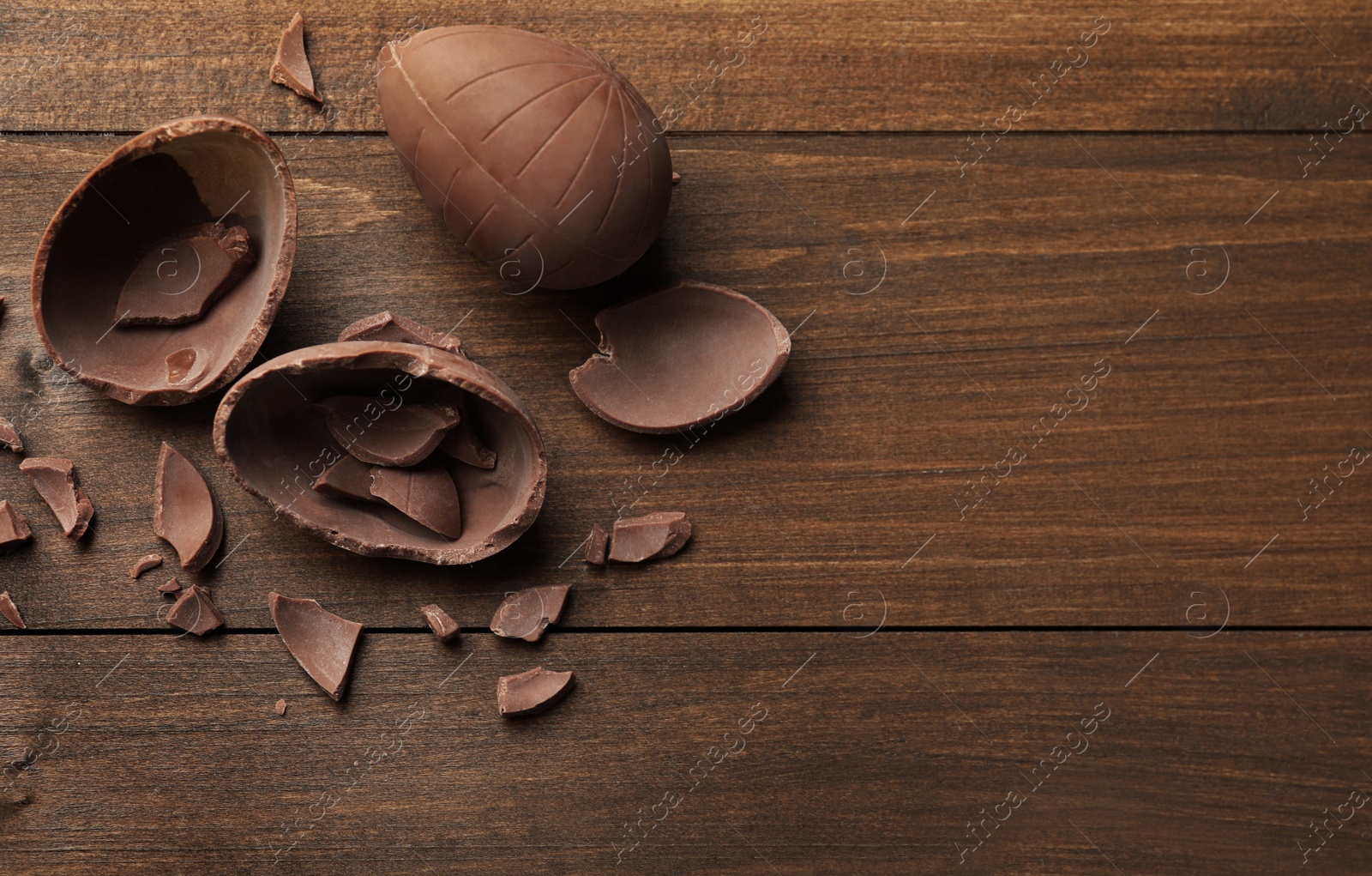 Photo of Broken chocolate eggs on wooden table, flat lay. Space for text